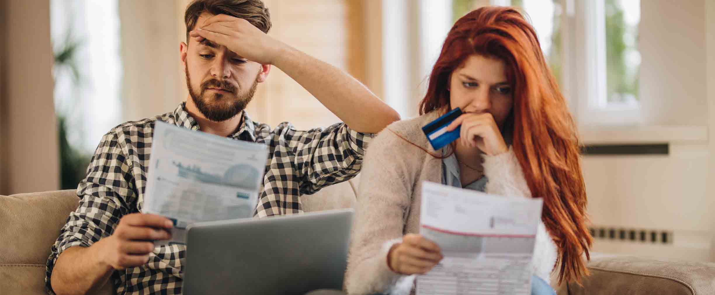Worried couple feeling frustrated while holding a credit card and looking at a computer and bills