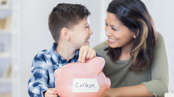 mom smiling at son as he drops change into a piggy bank