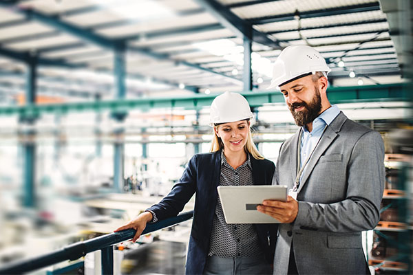 man and woman wearing white hard hats looking at a tablet