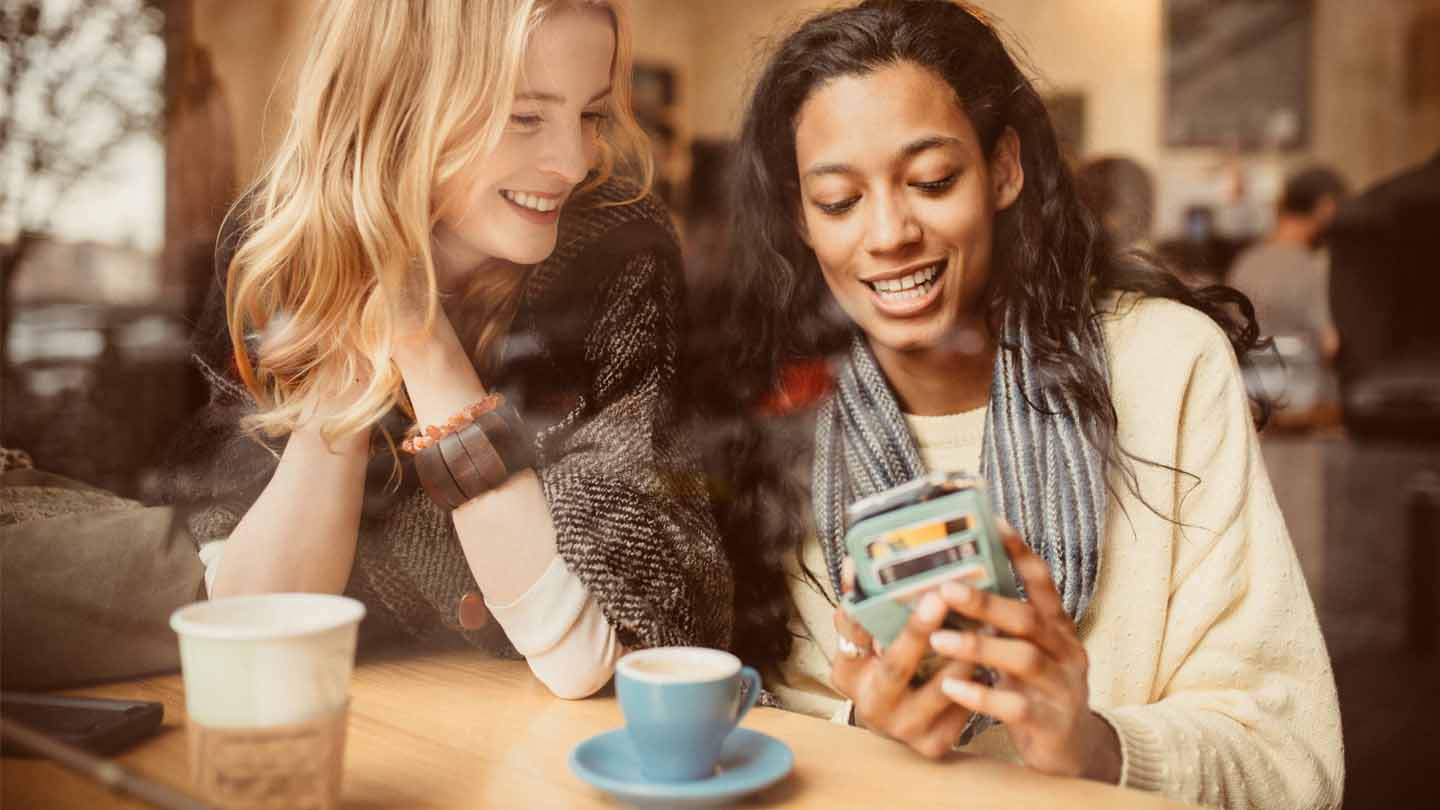 dos muchachas en una cafetería mirando un teléfono
