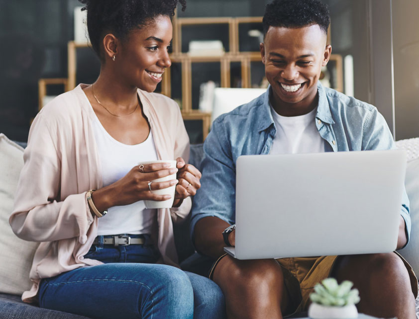 Pareja sentada en sofá mirando la pantalla de una laptop