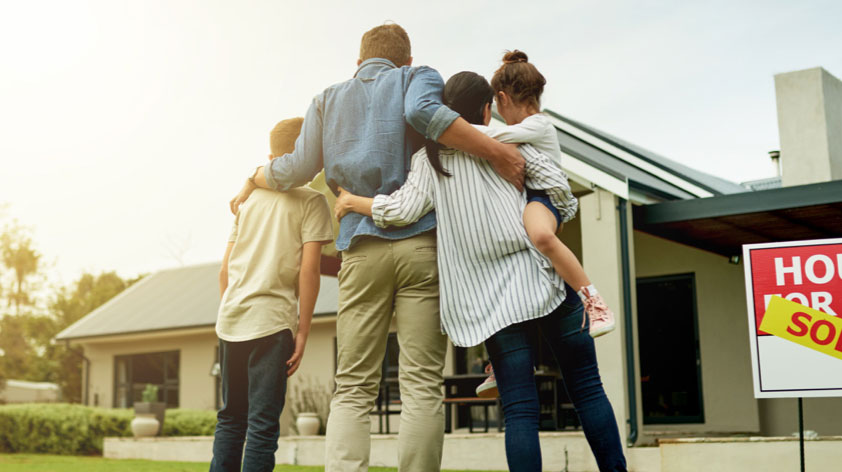 Familia abrazada mirando una casa vendida