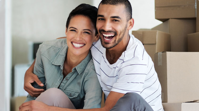 Smiling couple sitting in room with unpacked boxes