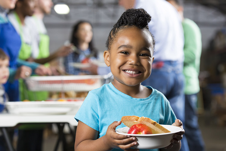 little girl smiling and holding bowl of food at food bank
