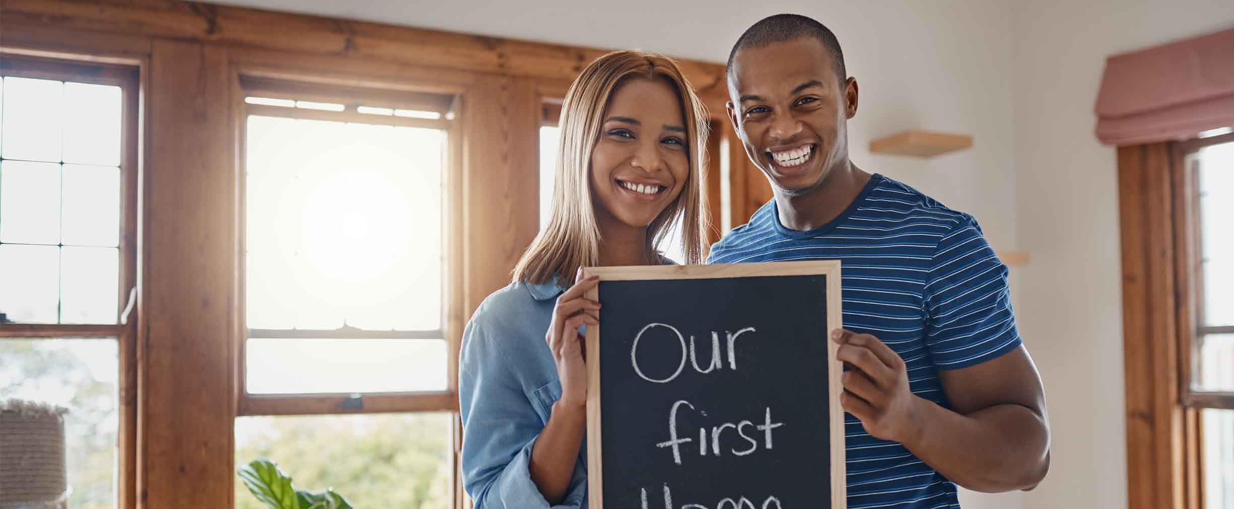 pareja feliz sonriente sosteniendo un cartel que dice nuestra primera casa