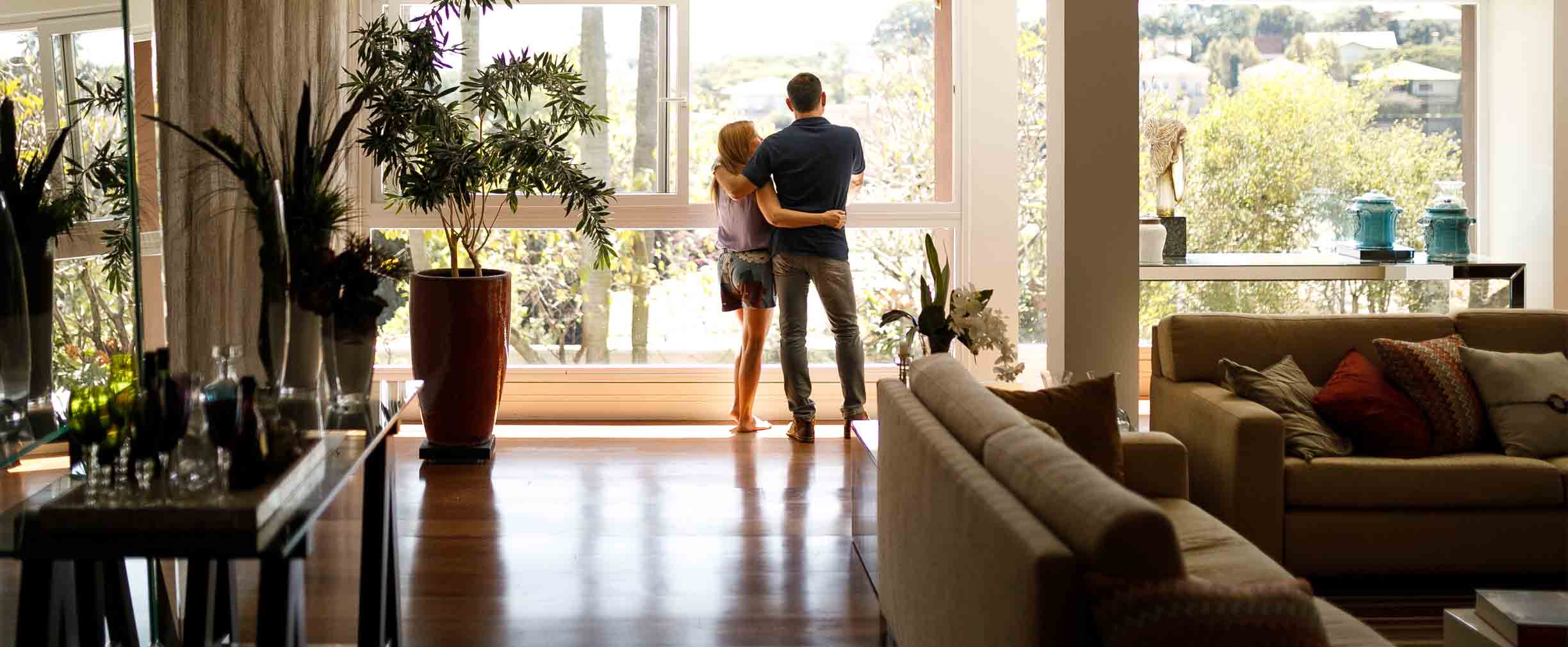 pareja abrazada en su sala mirando por la ventana