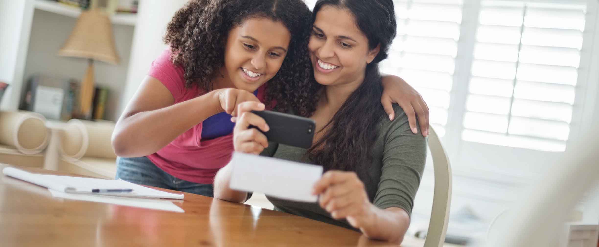 hija ayudando a su madre a depositar un cheque a través de un smartphone