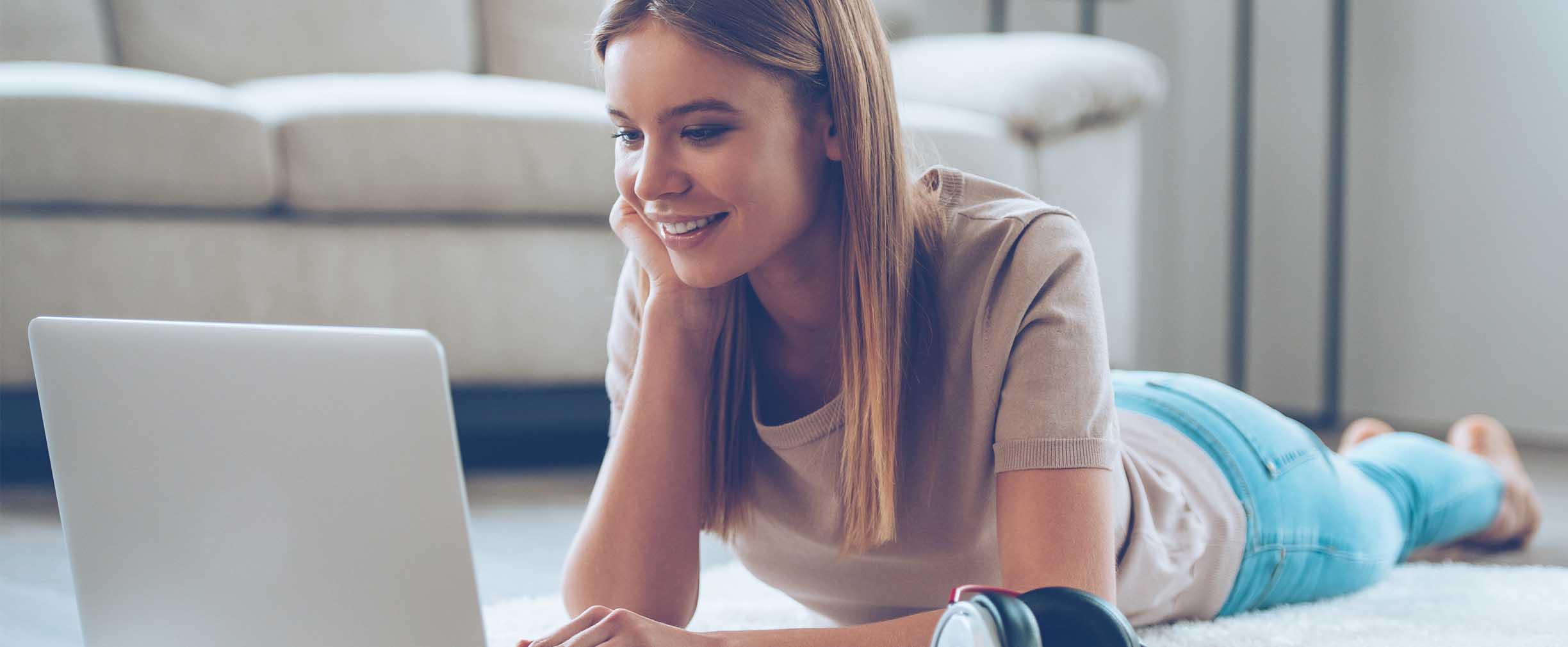 young female student sitting on the floor looking at her laptop