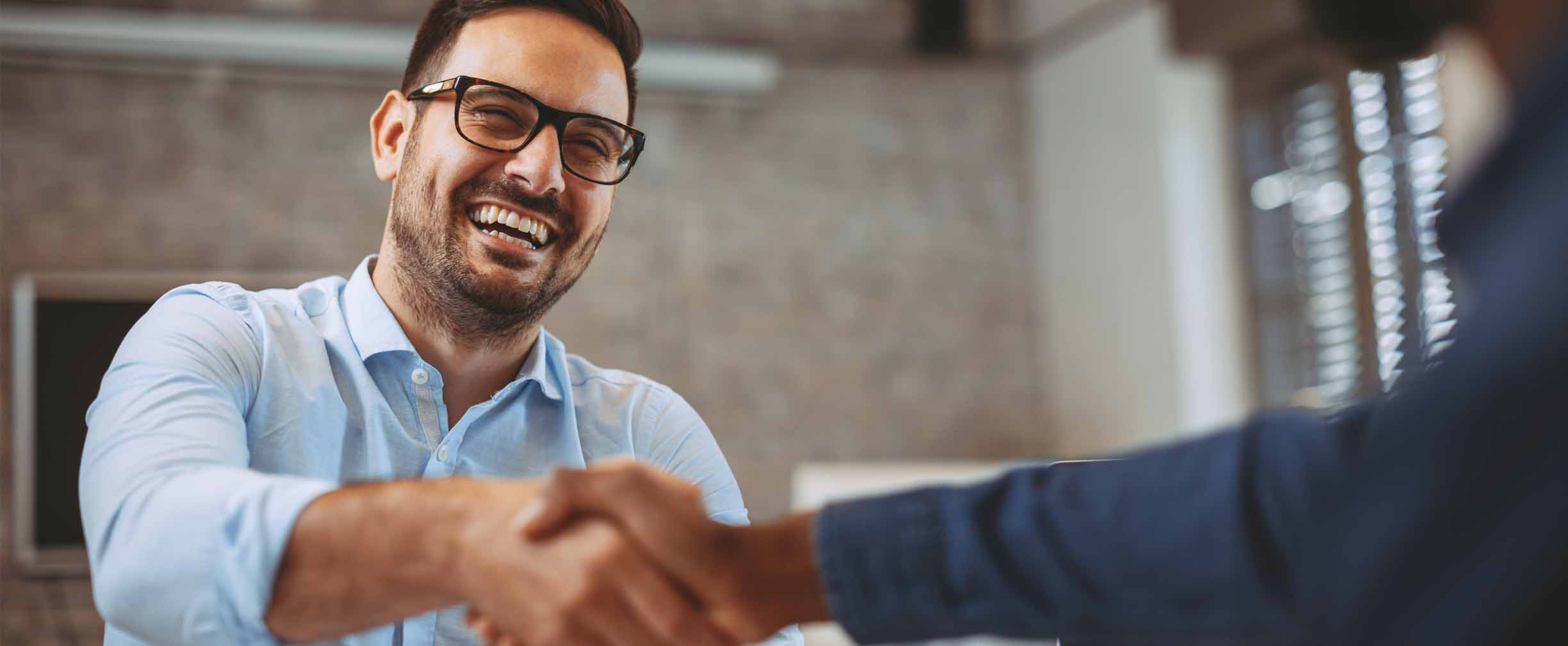 joven profesional masculino sonriéndo y estrechando manos con un colega