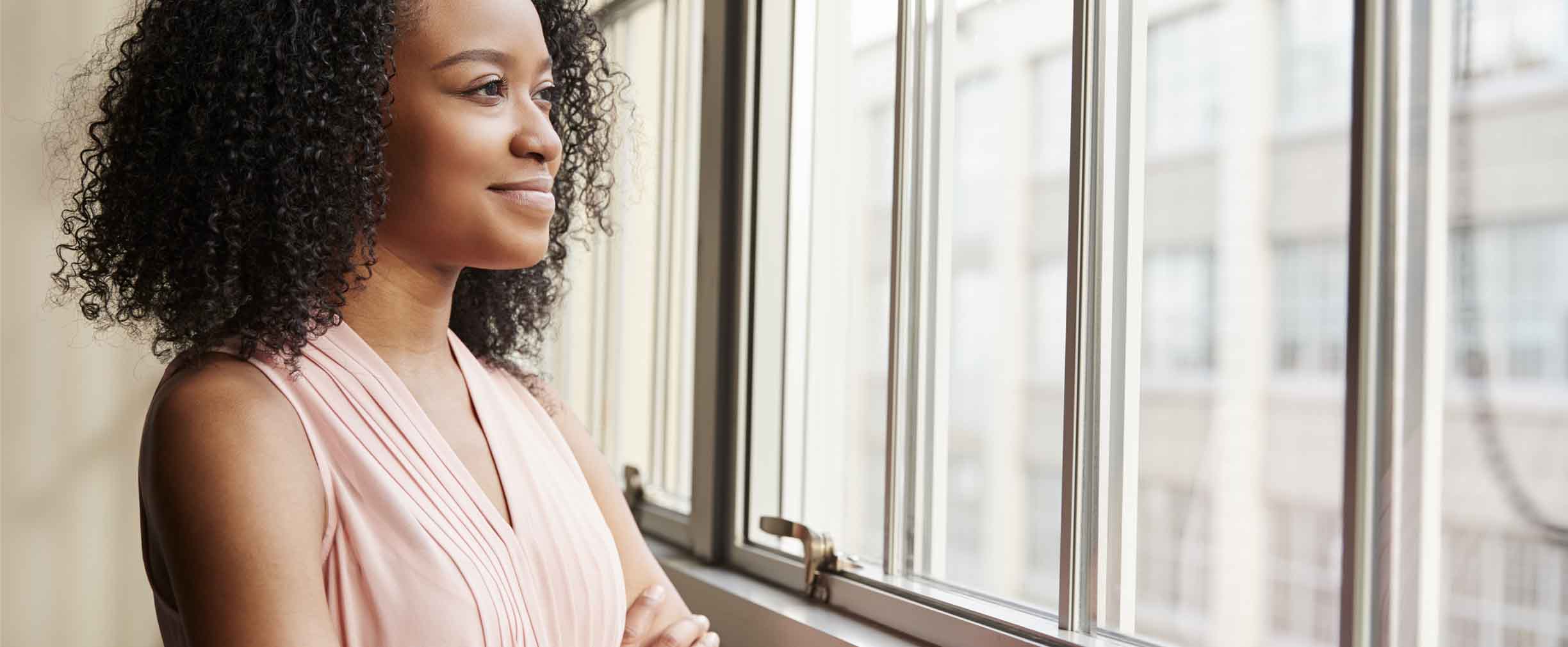 Young black woman with arms crossed looking out of window