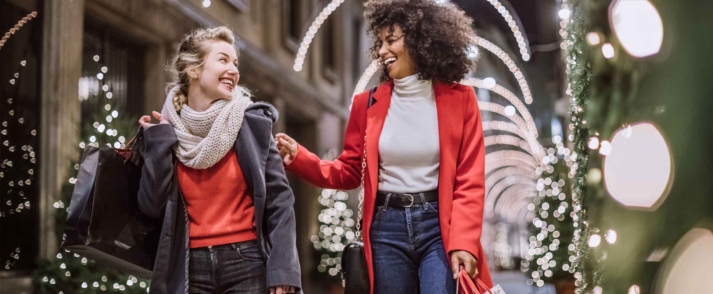 dos mujeres jóvenes haciendo las compras para las fiestas y llevando bolsas de compras