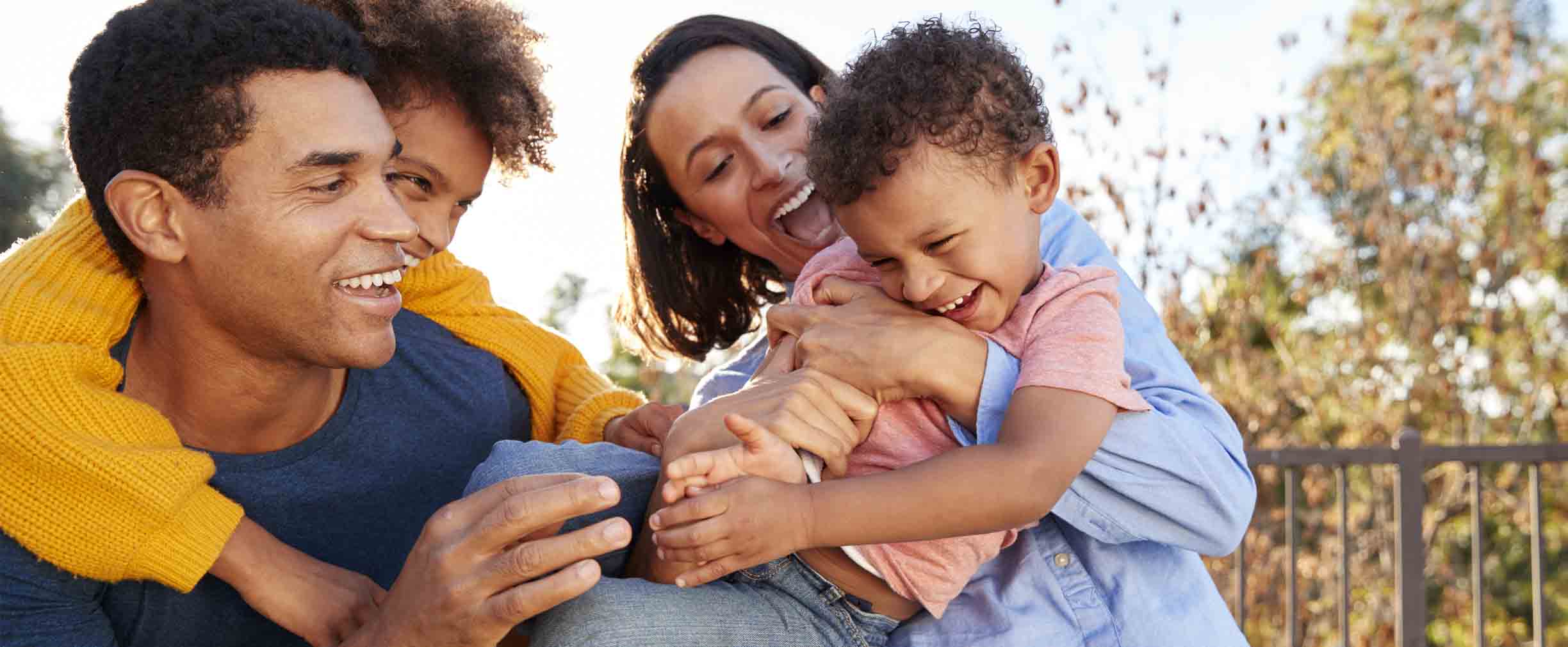 Young mixed race parents playing outdoors carrying their children in the garden