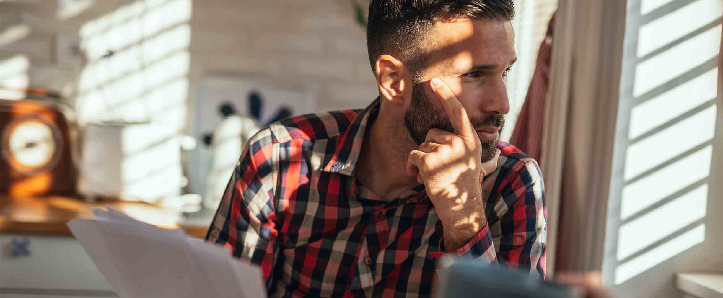 Stressed man sitting in the kitchen and holding papers