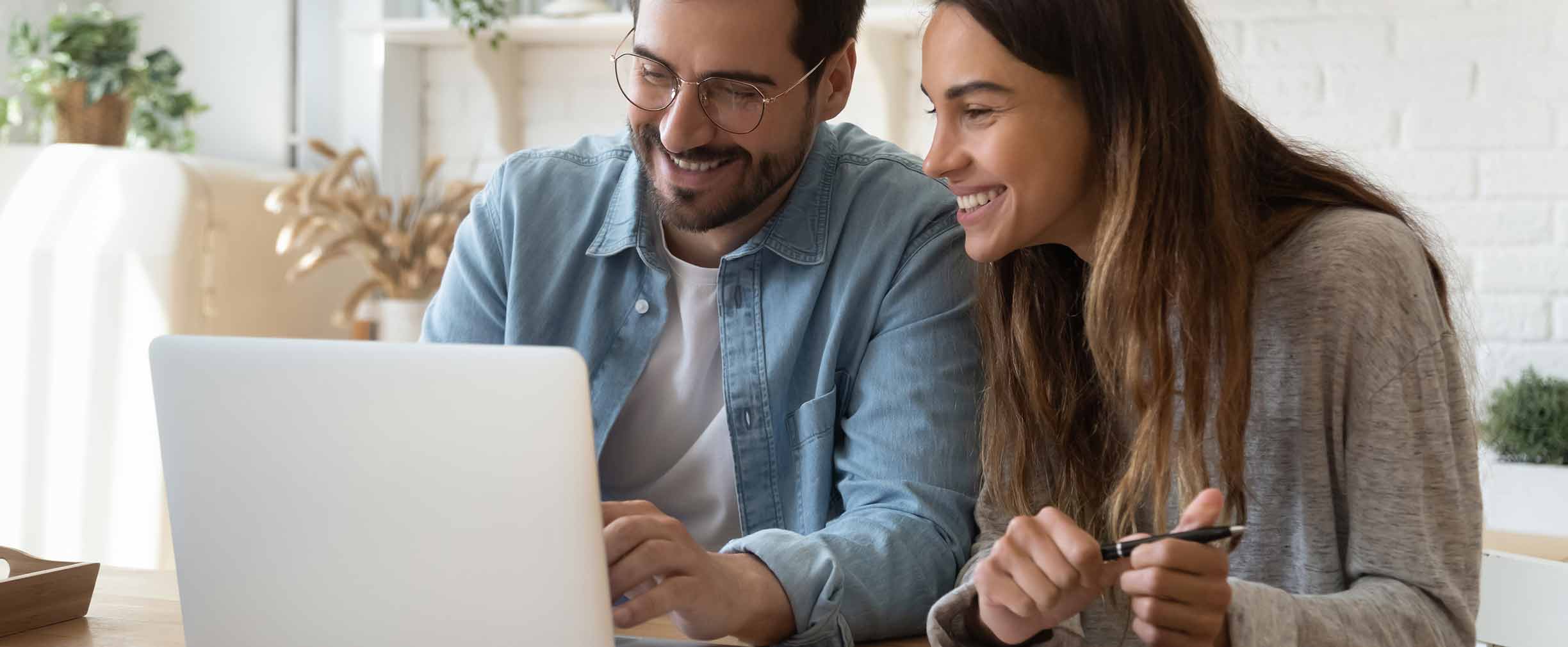 Pareja joven feliz usando laptop en casa.