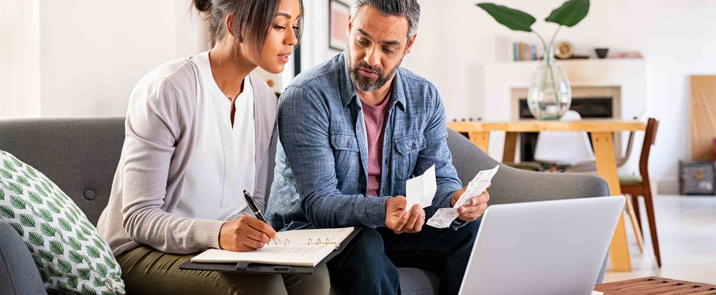 Pareja adulta calculando facturas en casa con una laptop y calculadora.