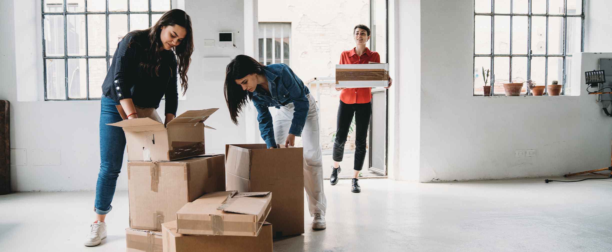 A small business owner and two of her employees unpack boxes in a sunlit new office space.