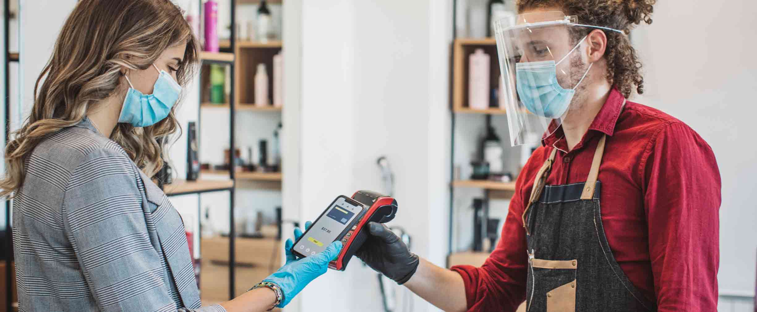 Mujer joven pagando el corte de pelo a su estilista durante el período de aislamiento por la pandemia, ambos usan guantes como protección