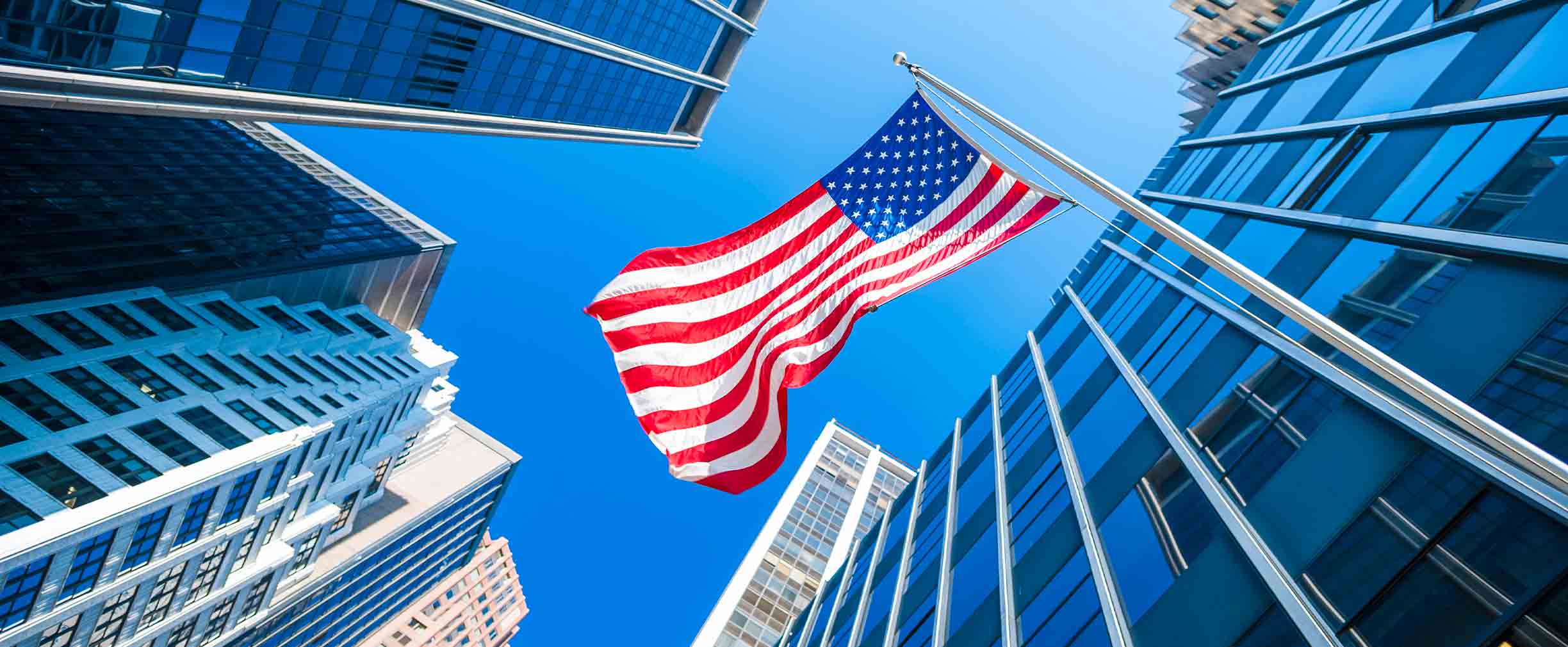 View of an American flag blowing in the wind, with tall buildings around it.