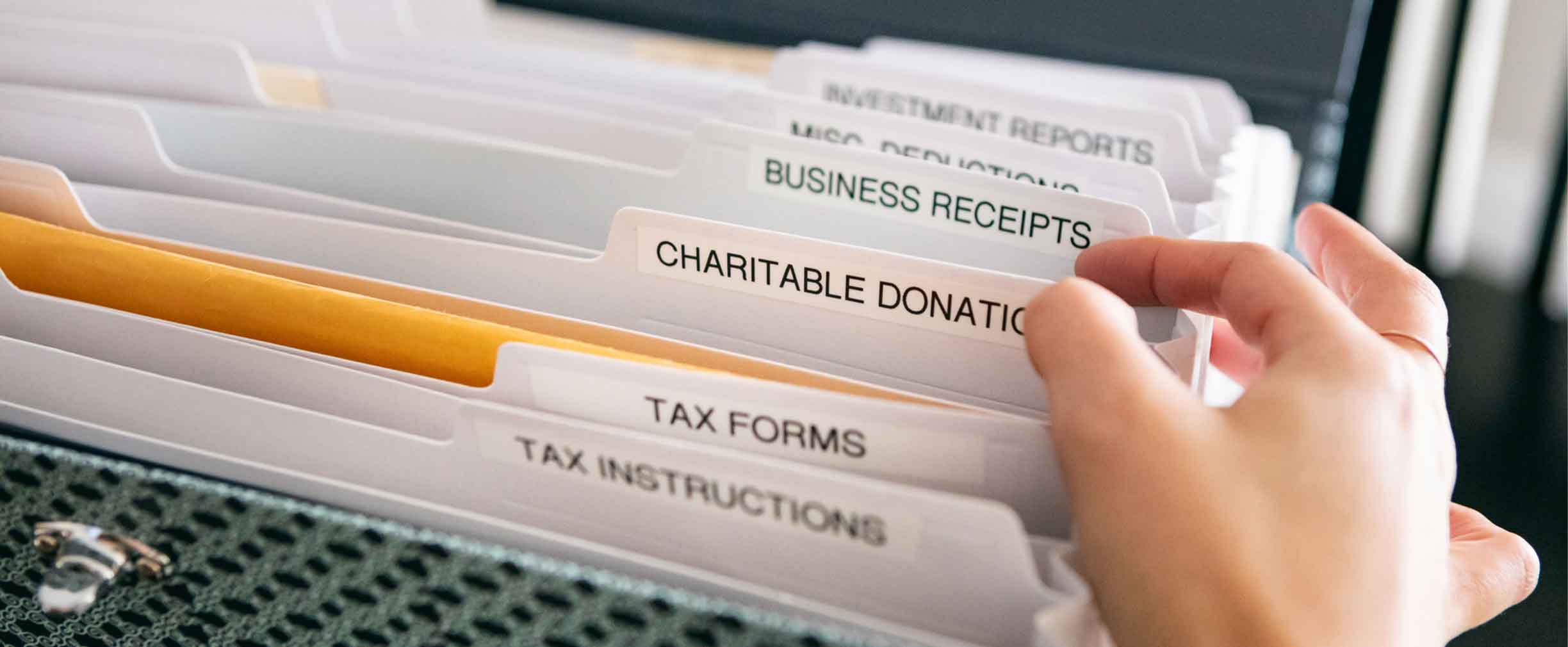 A person searching through a file cabinet with tax forms.