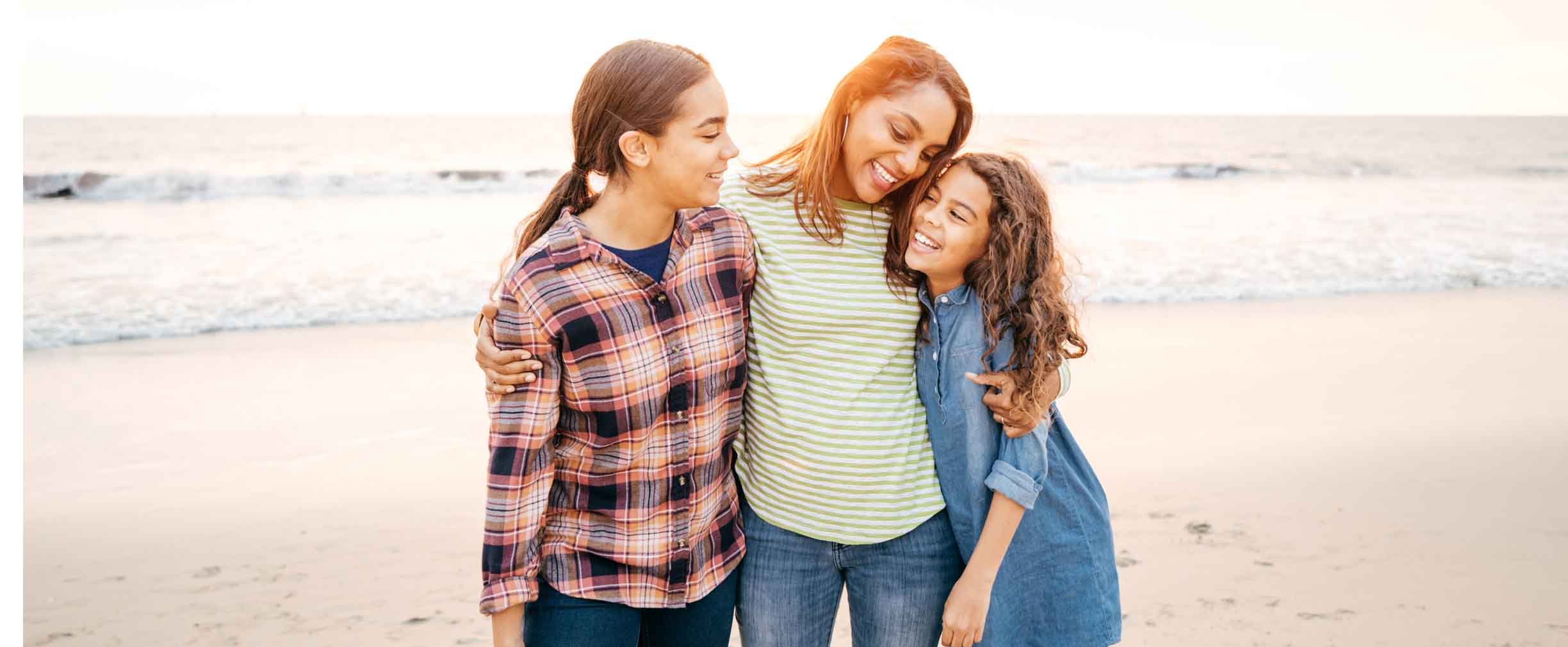 madre abrazando a sus dos hijas en la playa