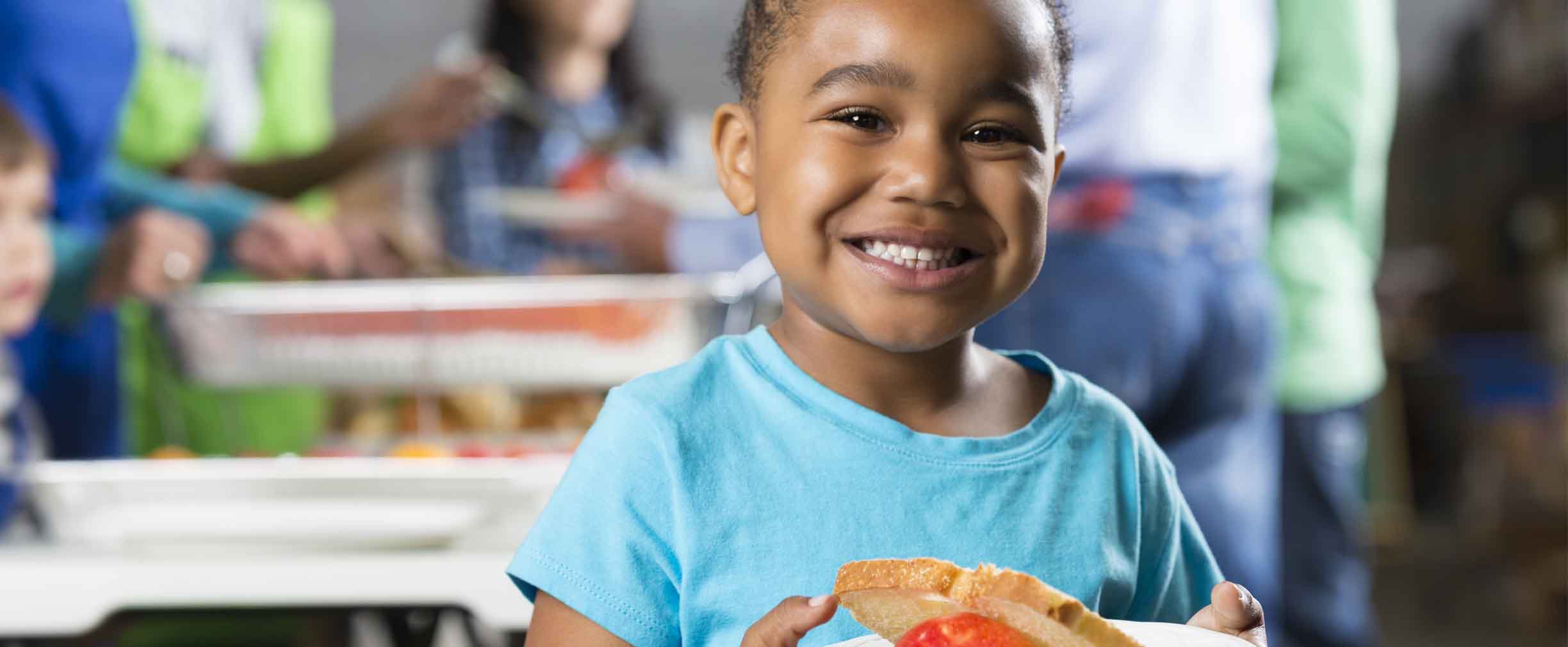 niña pequeña sonriente sosteniendo un tazón de comida en un banco de alimentos