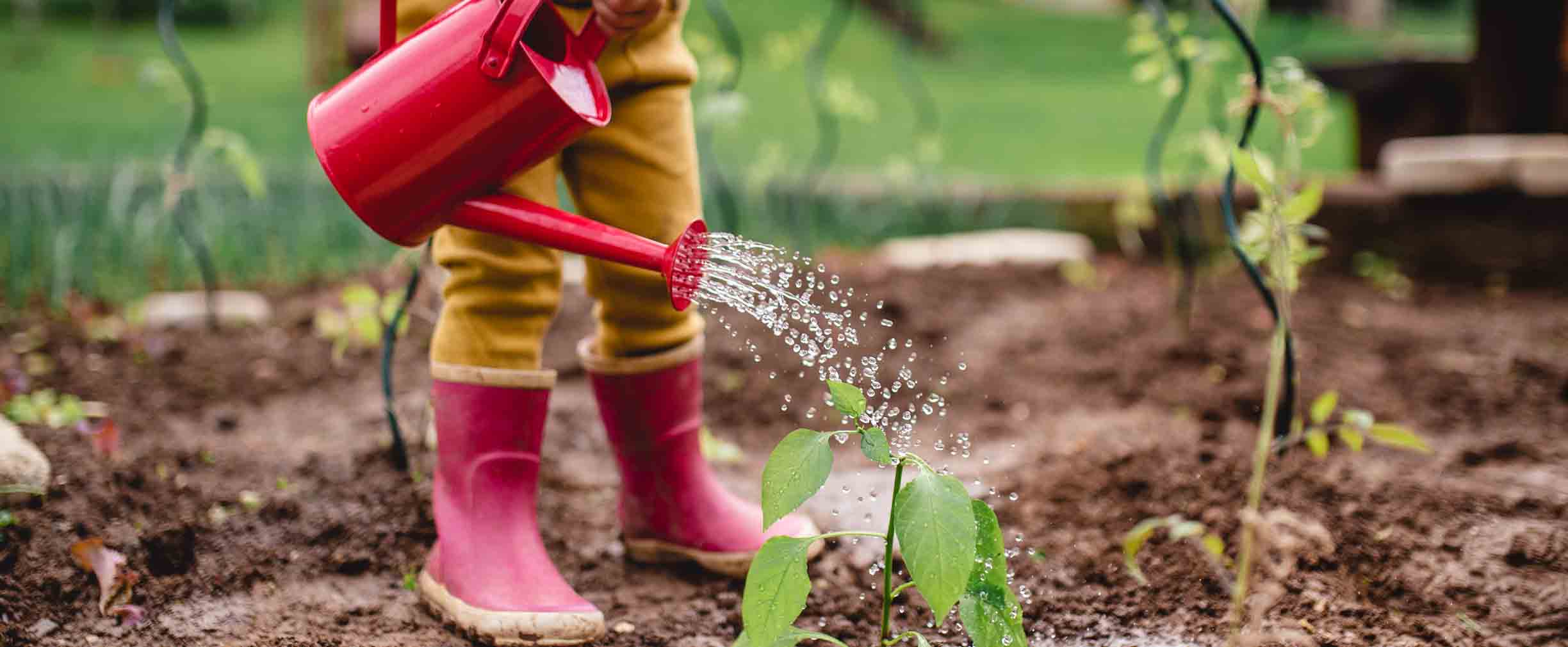 niño con botas de lluvia regando plantas