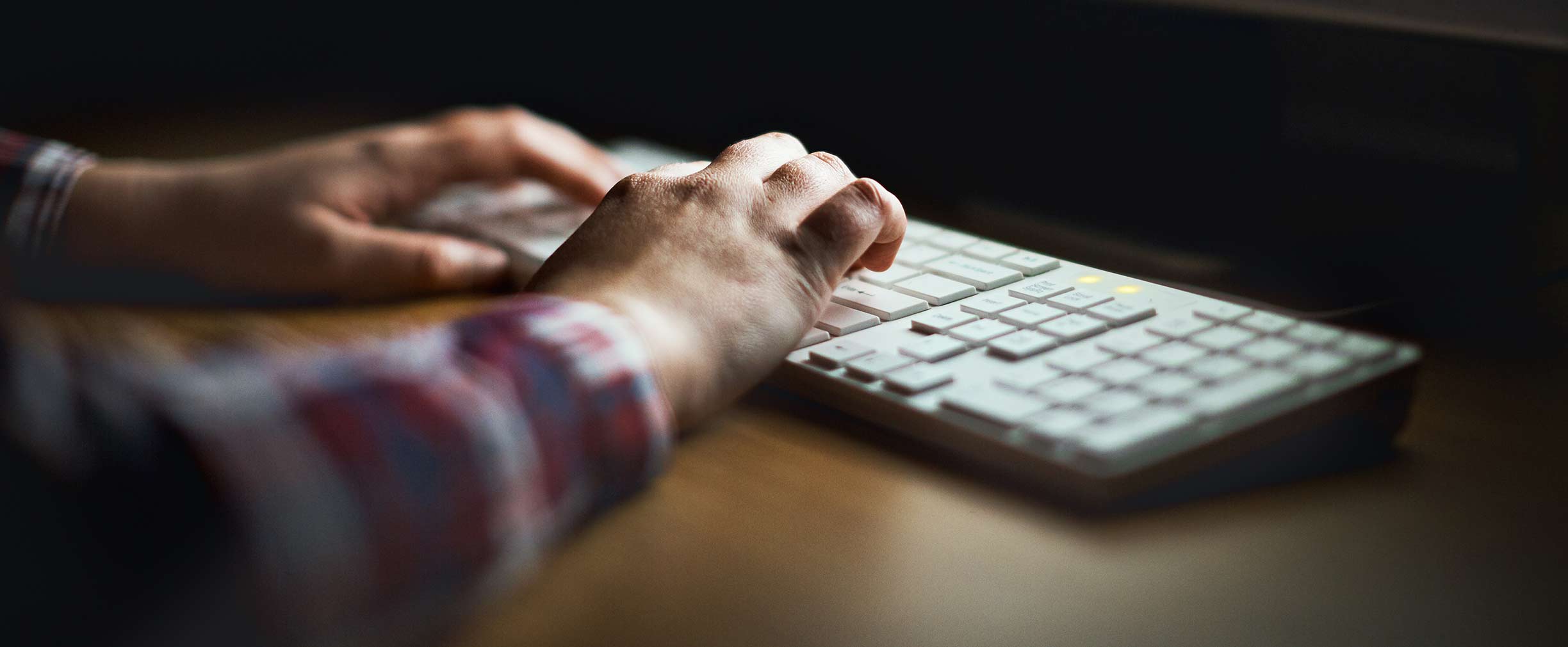 Manos que escriben en teclado de computadora iluminado por el monitor