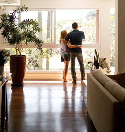 pareja abrazada en su sala mirando por la ventana