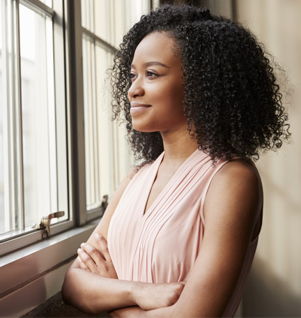 Young black woman with arms crossed looking out of window