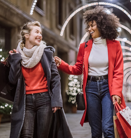dos mujeres jóvenes haciendo las compras para las fiestas y llevando bolsas de compras
