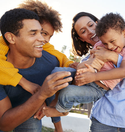 Young mixed race parents playing outdoors carrying their children in the garden