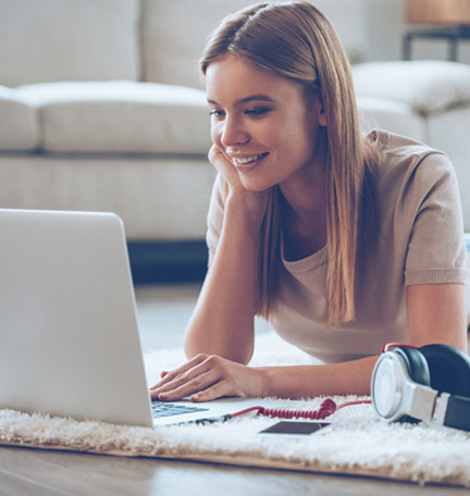 young female student sitting on the floor looking at her laptop
