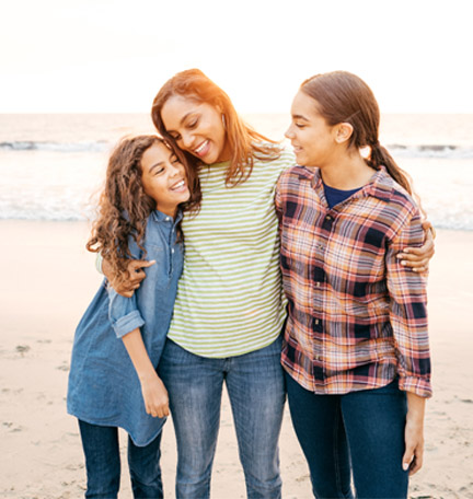 mother hugging her two daughters on the beach