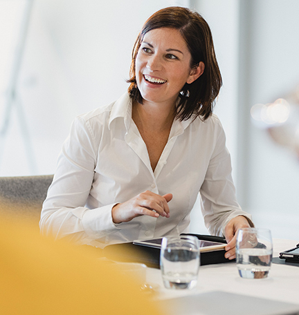 Empresaria sonriendo en una mesa de reuniones, escuchando, aprendiendo, éxito, felicidad