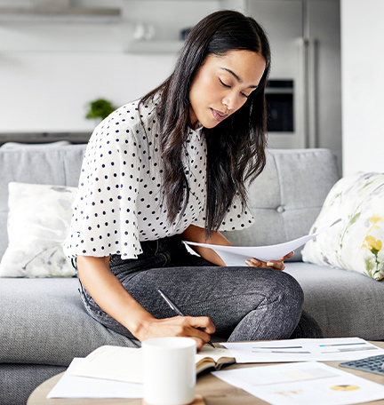 Young woman analyzing bills while writing in diary. Female is using digital tablet at table. She is sitting on sofa at home.