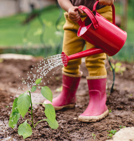 niño con botas de lluvia regando plantas